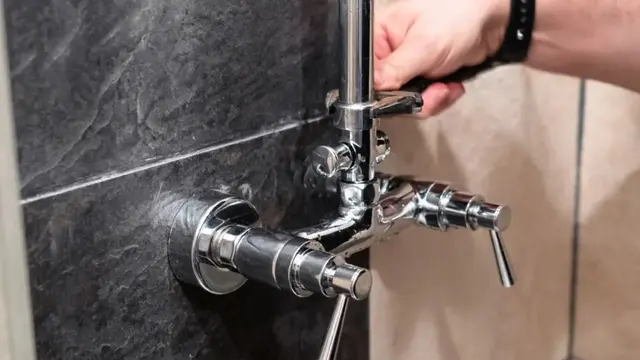 Hand working on the handles of a bathtub faucet on a tiled wall