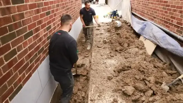 Workers excavating along a brick foundation wall to waterproof it from outside